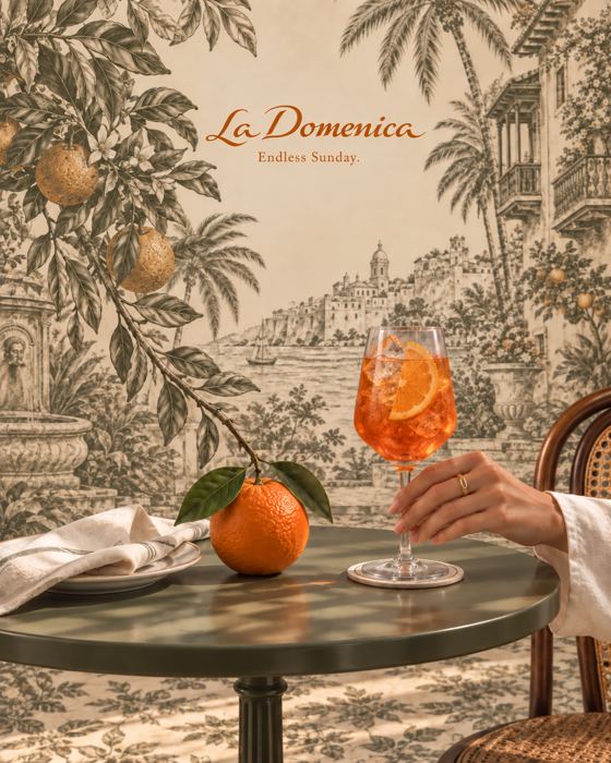 Un spritz y una naranja sobre una mesa, frente a un toile