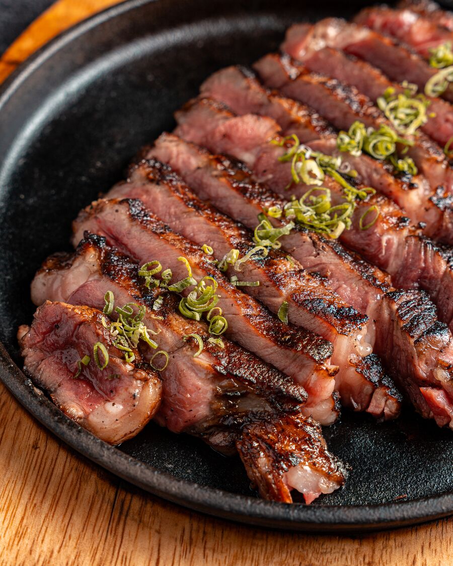 Carne a la brasa en láminas con cebollín sobre plancha de hierro