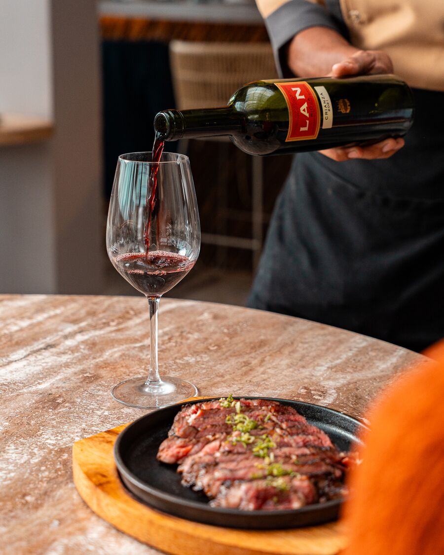 Mesero sirviendo vino tinto junto a un plato de carne