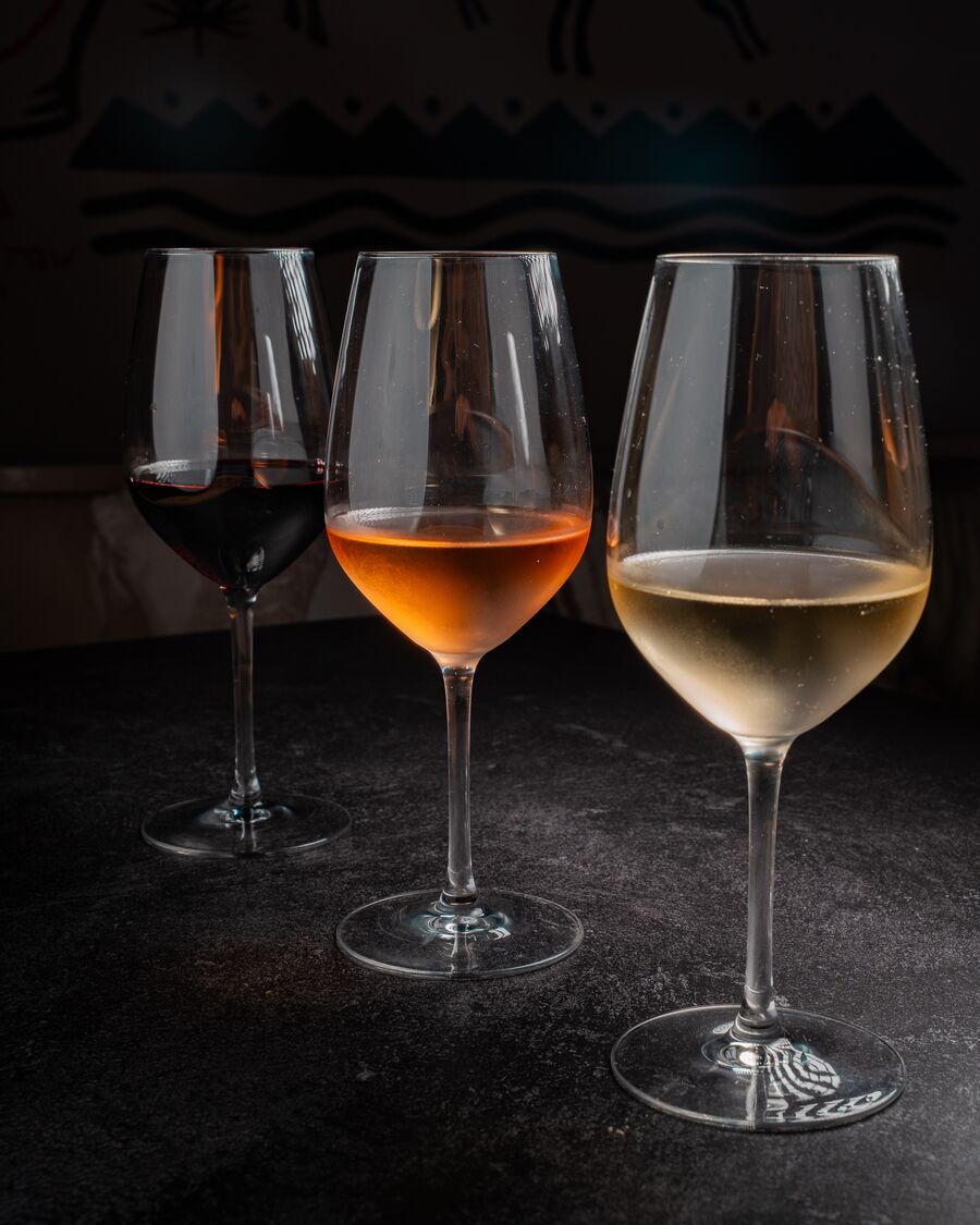 Tres copas de vino tinto, naranja y blanco sobre fondo oscuro